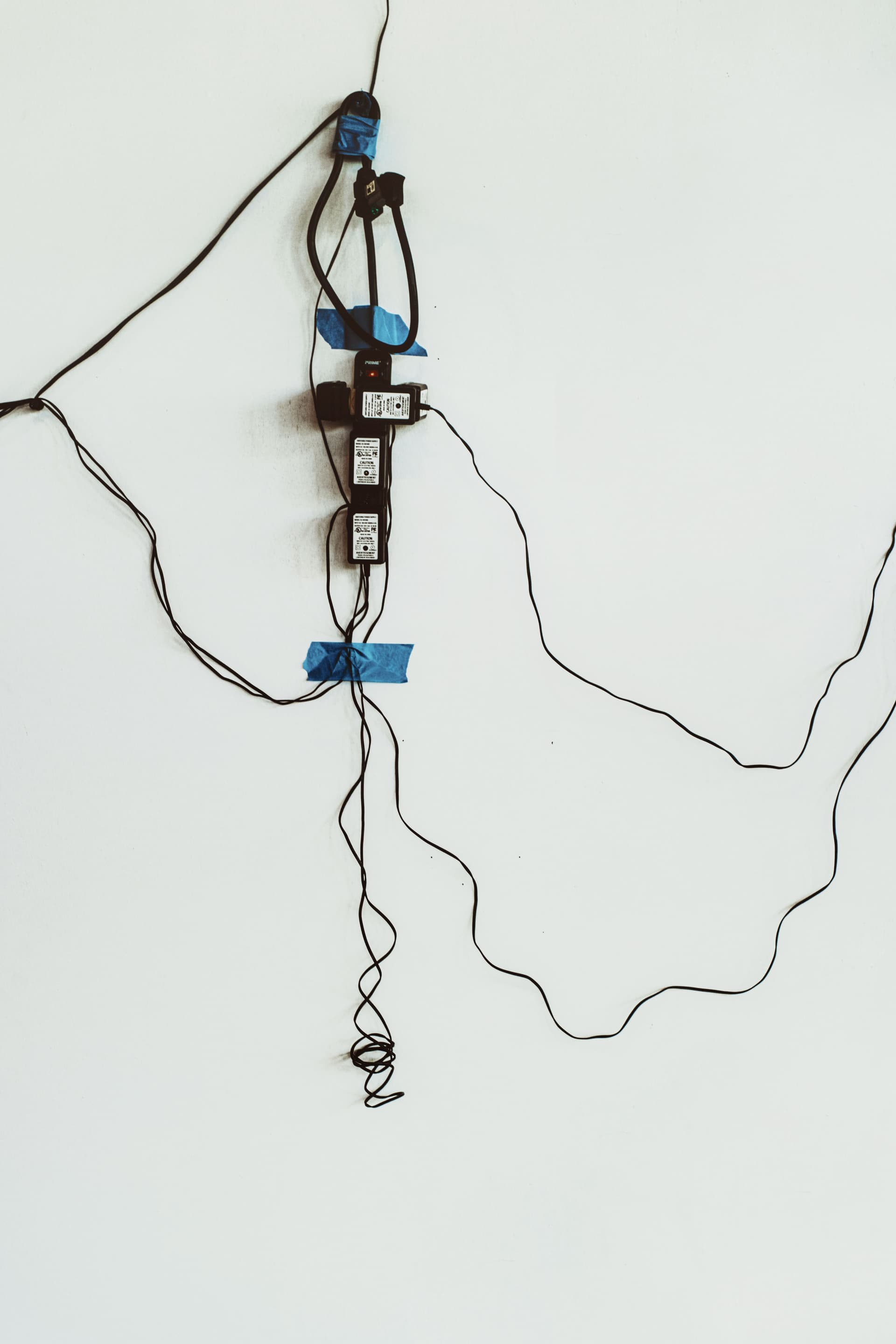 Tangled cables and several power sockets taped to a wall.