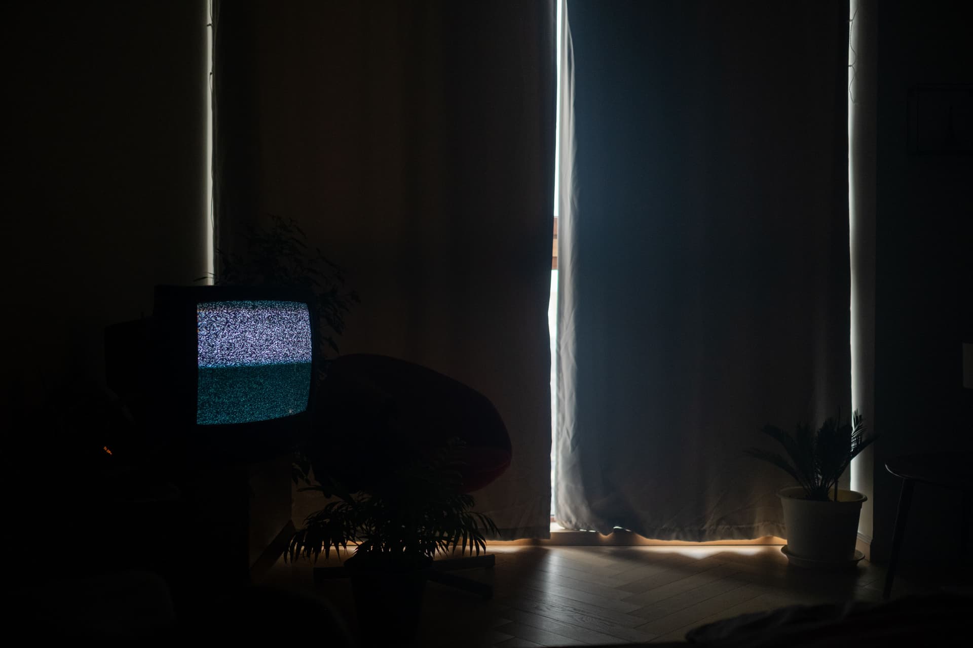A dimly lit living room with static on the television and the curtains drawn.